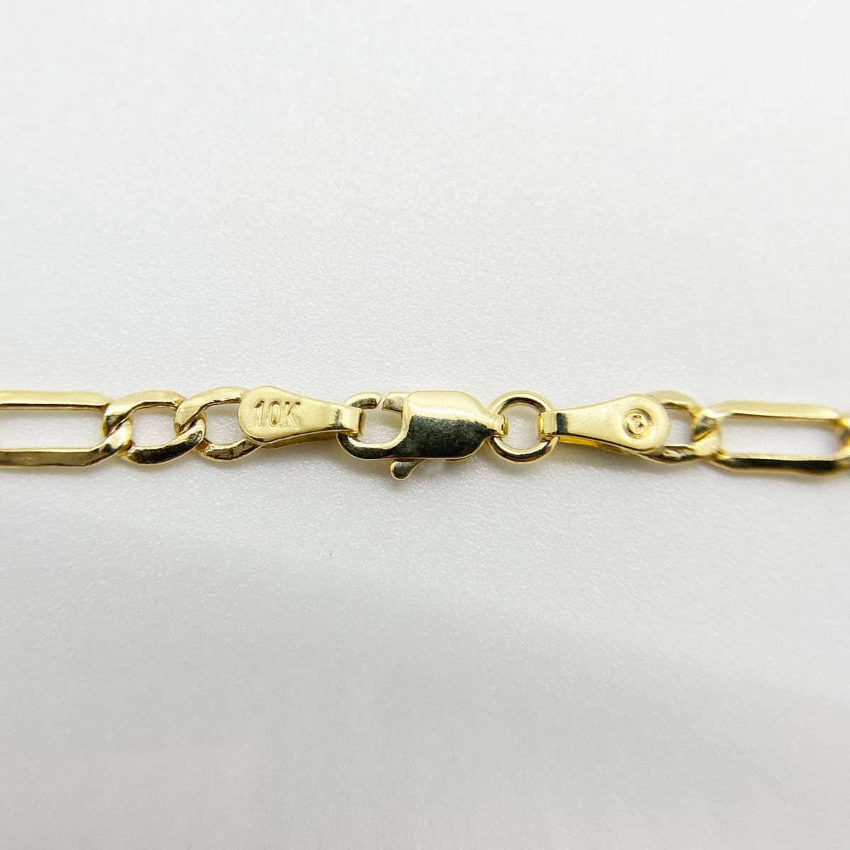Close-up of 10k gold Figaro chain showing lobster clasp and stamped end link.