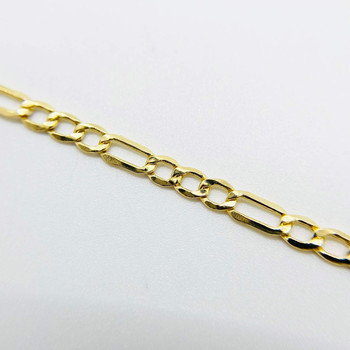 Close-up view of a polished 14k gold Figaro chain on a white background.