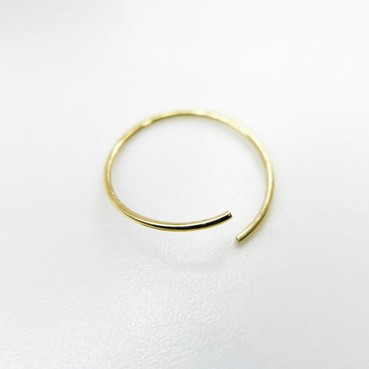 A thin, open-ended 14k gold nose hoop isolated on a white background.