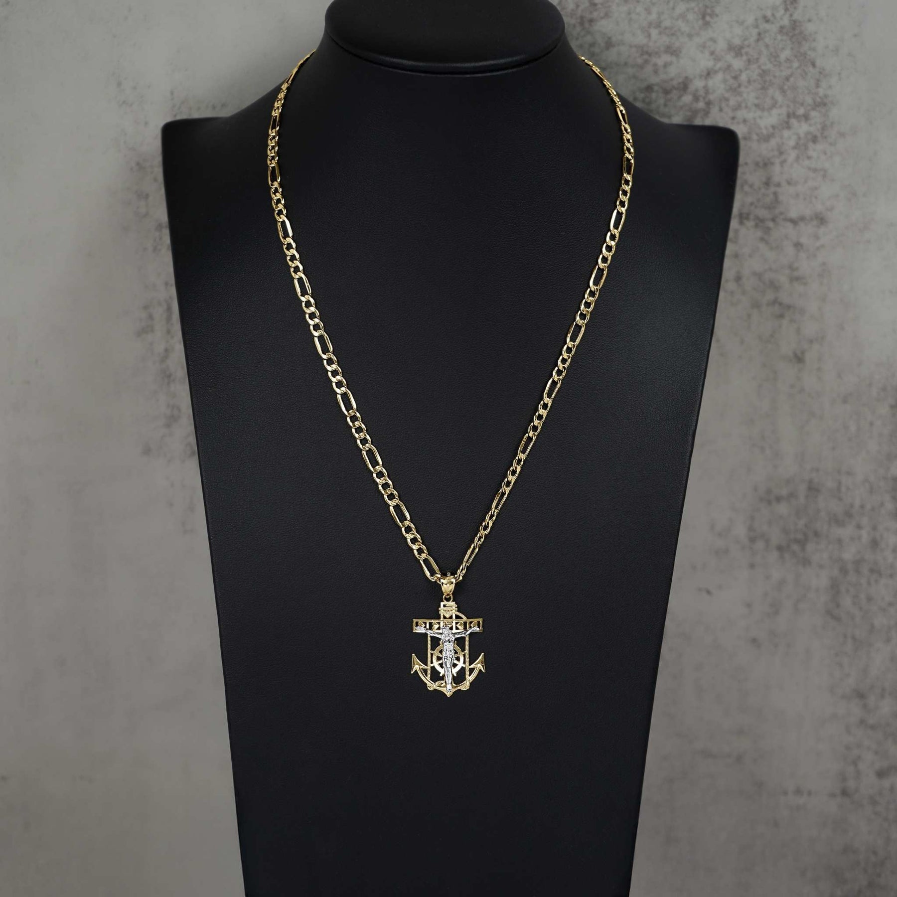 A gold chain necklace with a crucifix anchor pendant displayed on a black mannequin bust