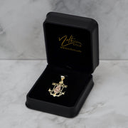 Two-tone gold Guadalupe anchor pendant inside an open black jewelry box on marble background