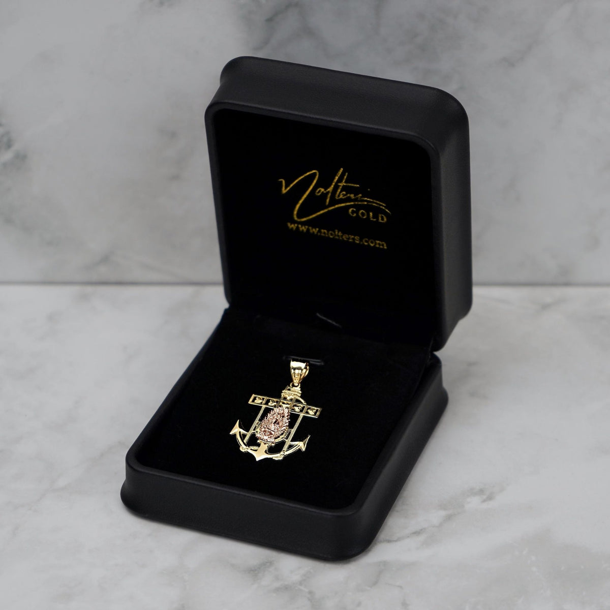 Two-tone gold Guadalupe anchor pendant inside an open black jewelry box on marble background