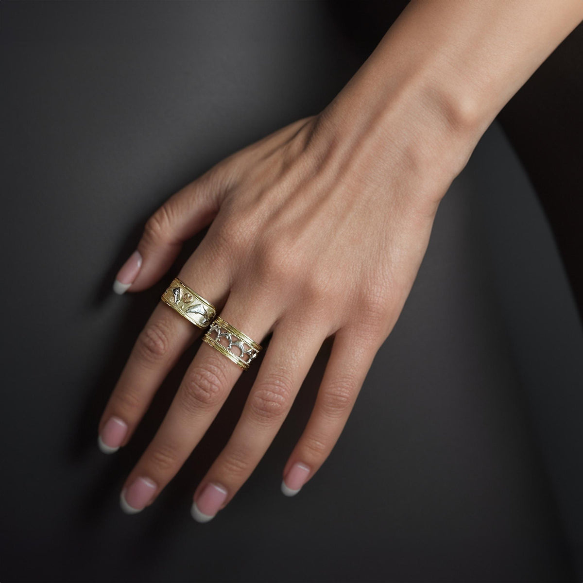 A woman’s hand wearing a two-tone 14k gold dolphin wide band ring.