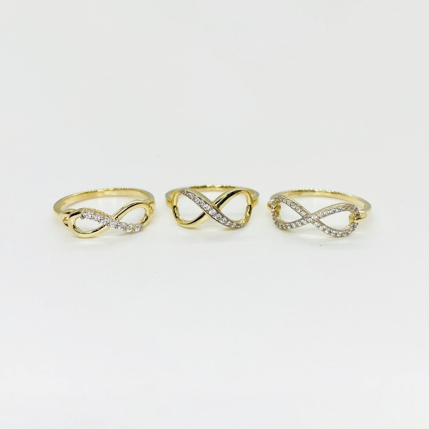 Three 14k gold infinity rings with Cubic Zirconia accents on a light gray background