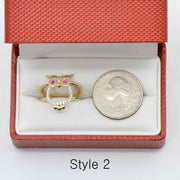 14k Gold owl ring with pink and white  Cubic Zirconia in a red jewelry box next to a silver coin.
