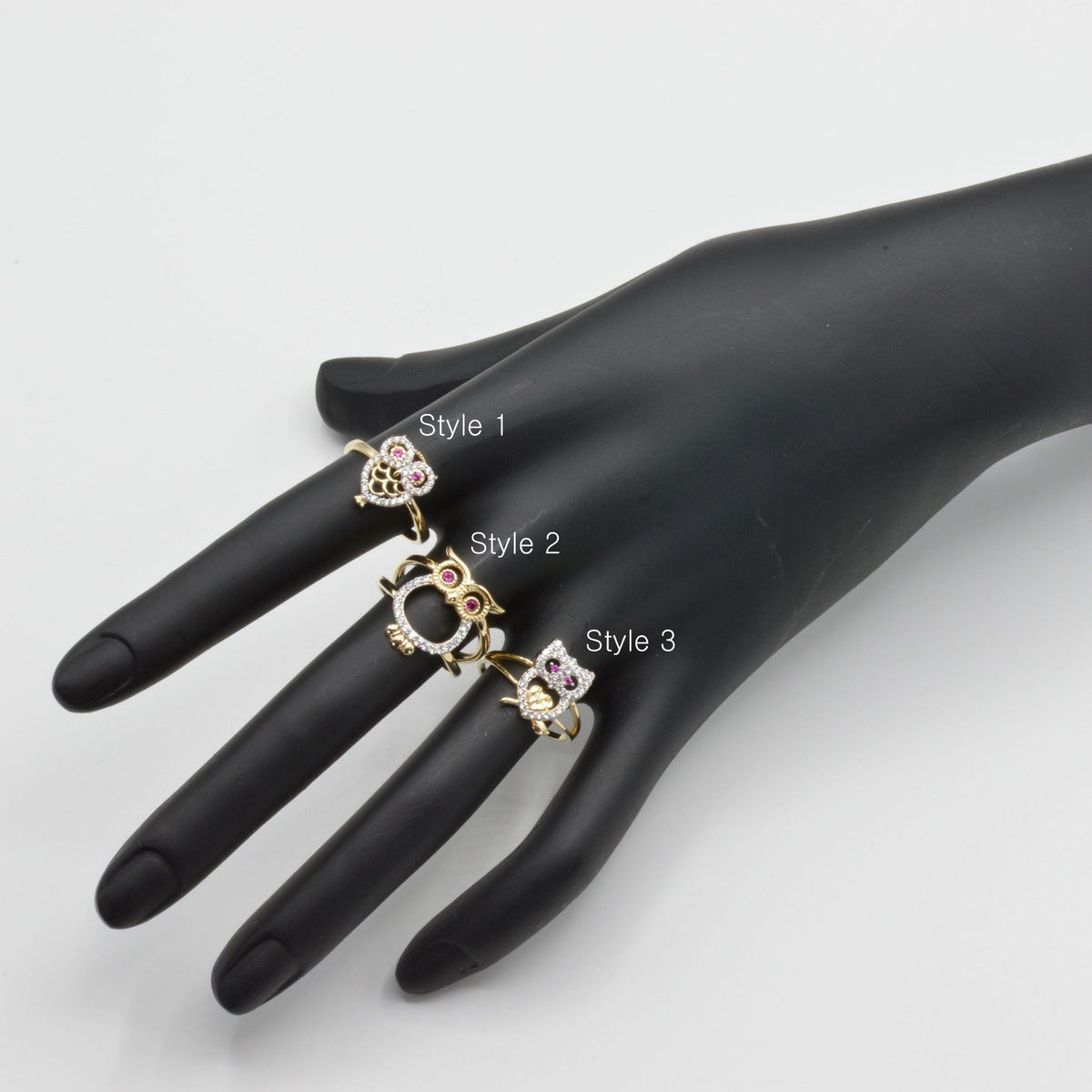 Three 14k gold owl rings with different designs on a black mannequin hand against a white background.