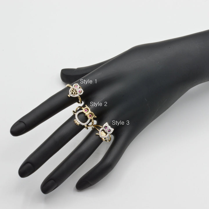 Three 14k gold owl rings with different designs on a black mannequin hand against a white background.
