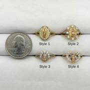 Four 14k gold Virgin Mary rings with different design next to a quarter.