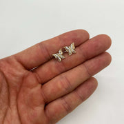 Pair of gold butterfly stud earrings encrusted with clear cubic zirconia held on an open palm.