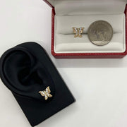 Gold butterfly earring on ear model beside another earring and a quarter for scale.