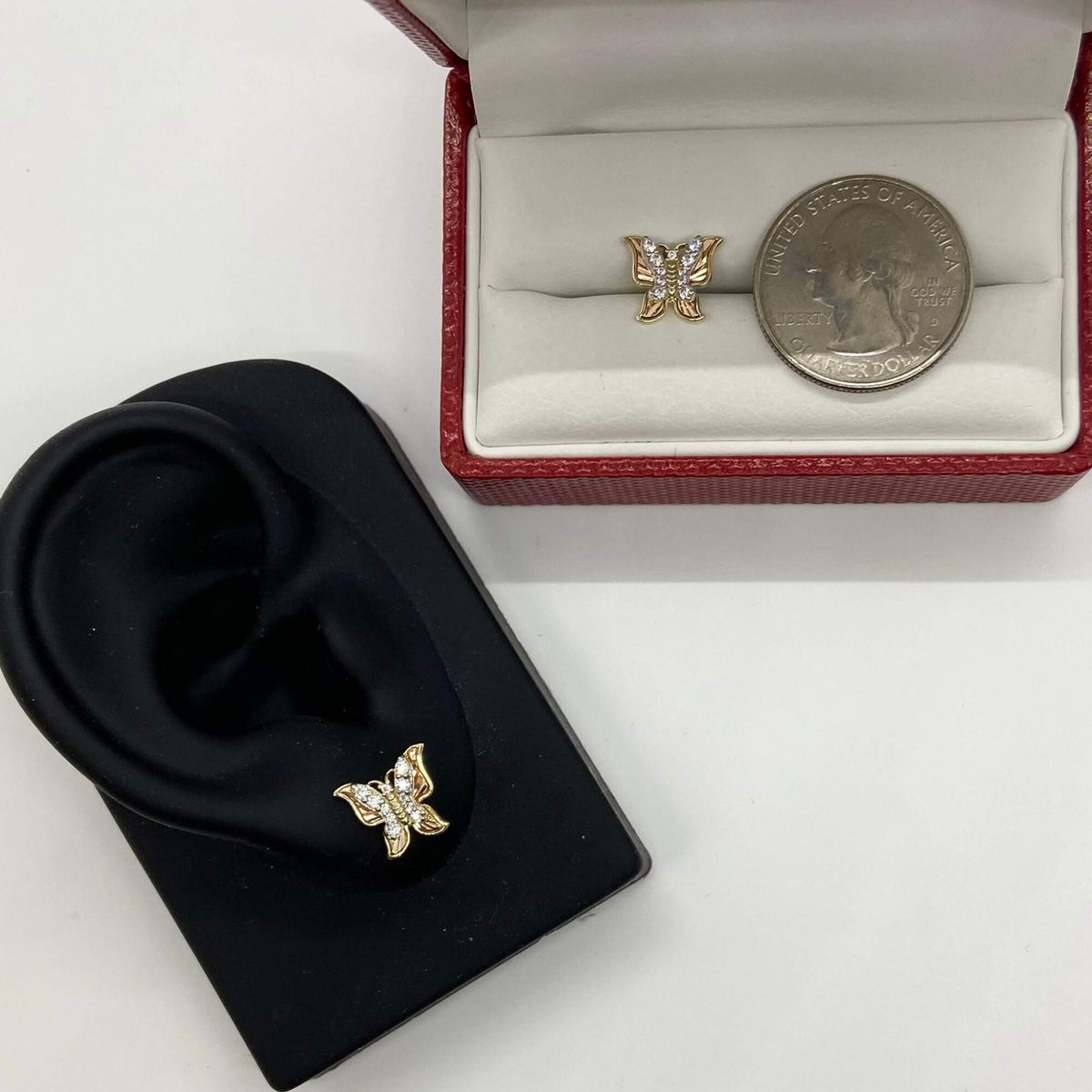 Gold butterfly earring on ear model beside another earring and a quarter for scale.
