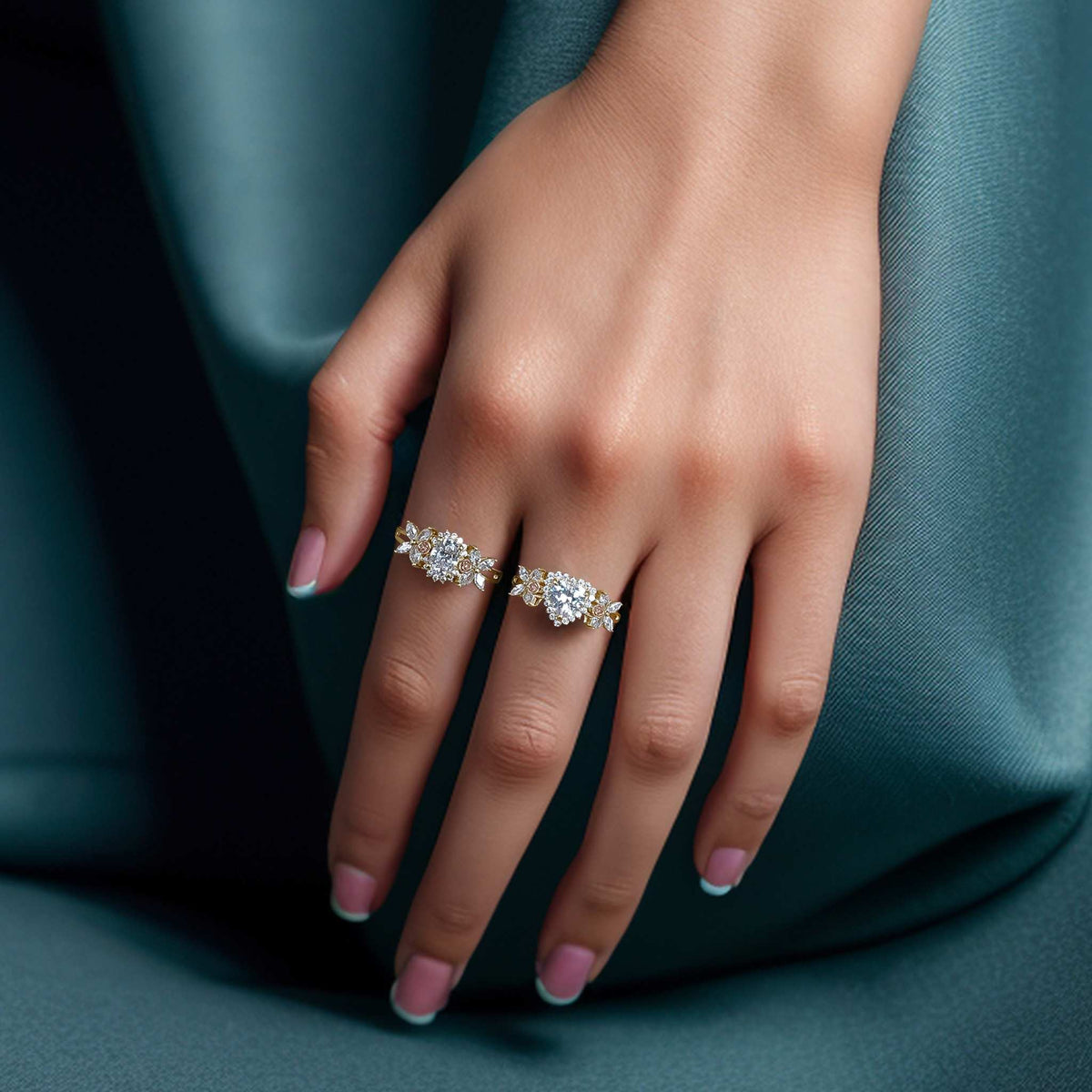 Hand wearing two 14k gold two-tone birthstone rings against a teal fabric background.