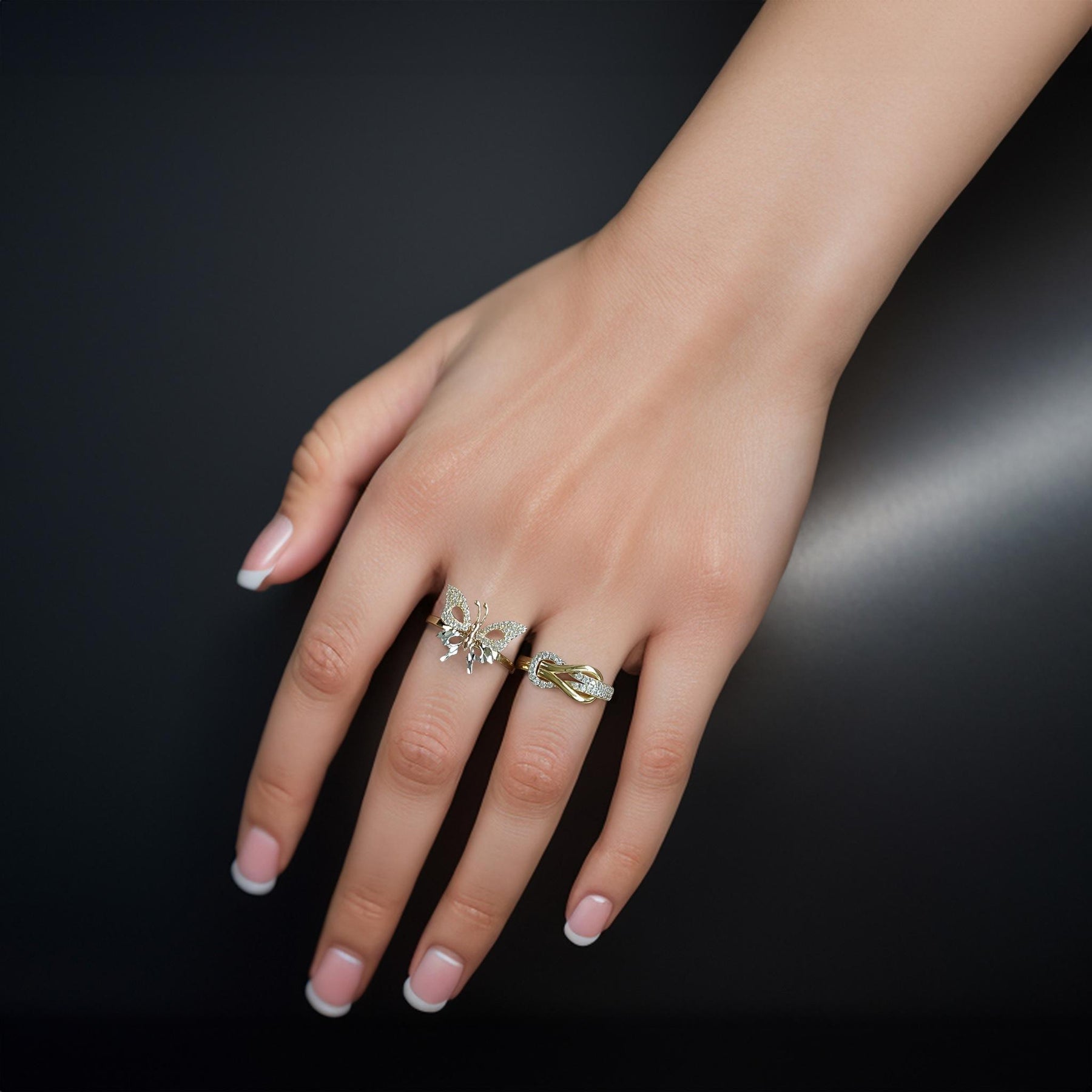 Two yellow gold statement rings styled on a hand against a dark background.