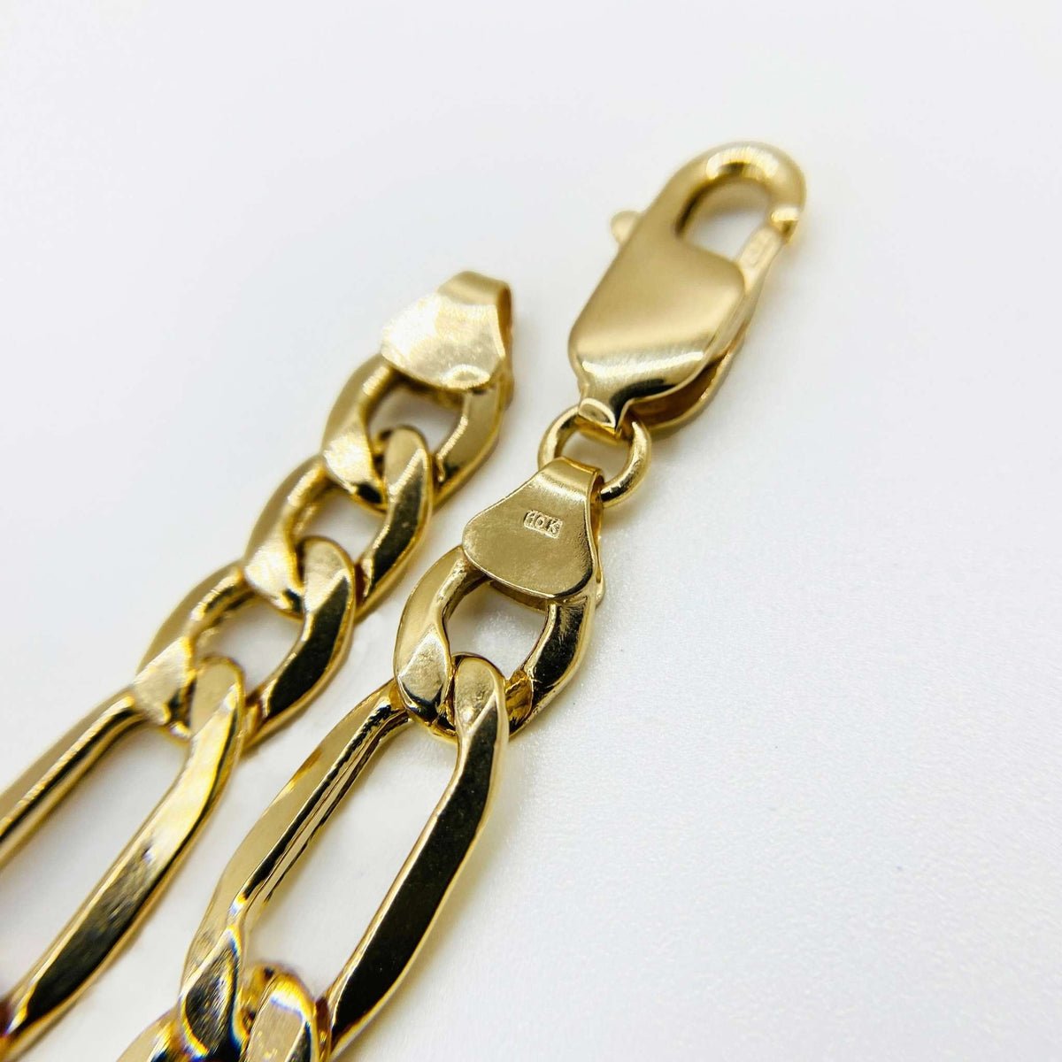 Close-up of a 14k gold Figaro chain showing the lobster clasp and stamp.