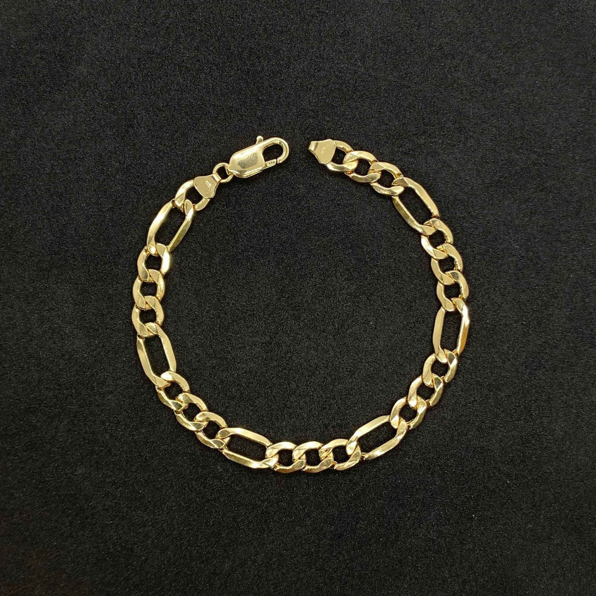 14k yellow gold classic Figaro link chain bracelet displayed on a textured black background.