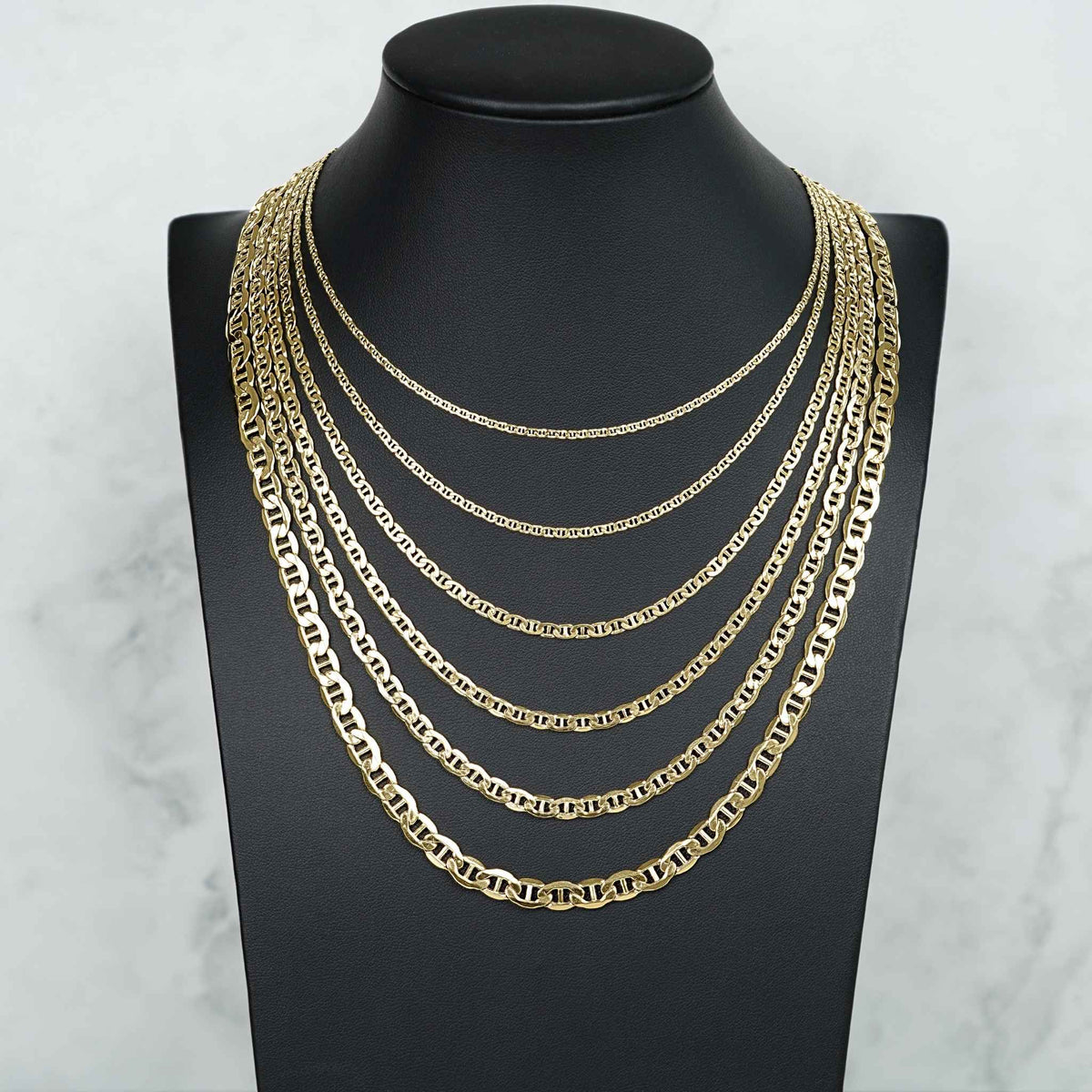 Five 14k yellow gold Mariner link chains displayed on a black neck bust model.