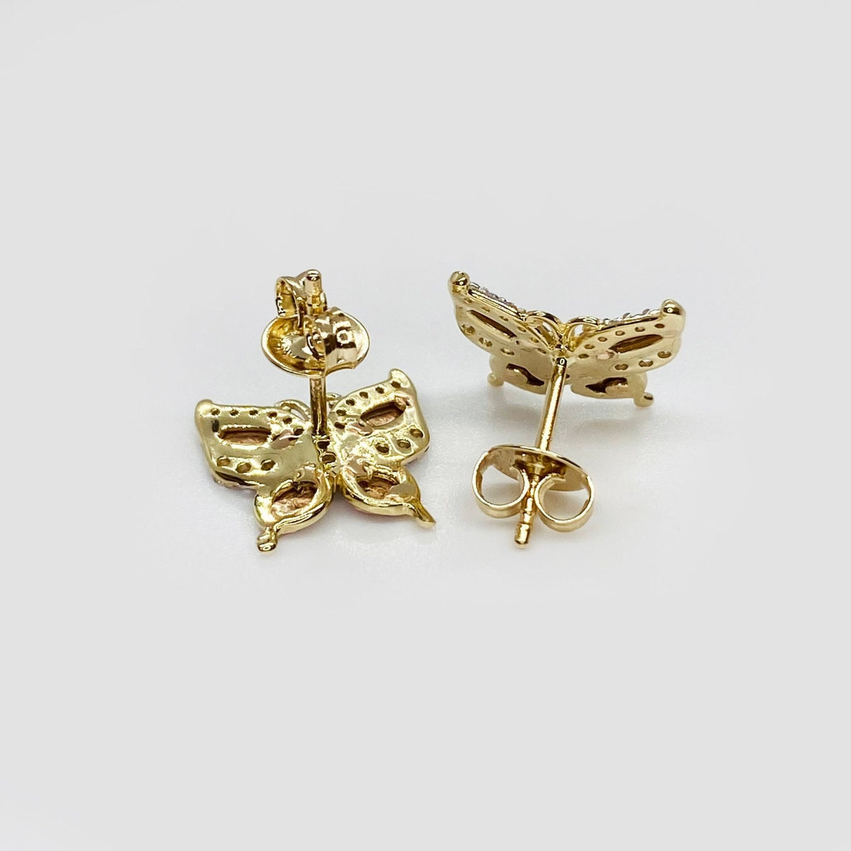 Rear view of gold butterfly stud earrings with push-back closures on white background.