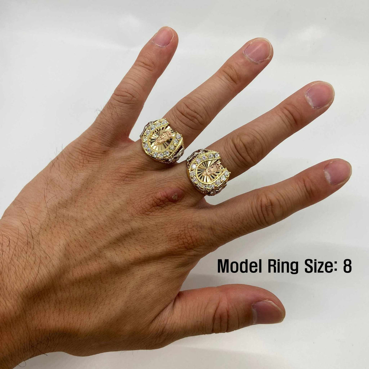 Hand wearing two 14k Horseshoe Virgin Mary gold rings with a plain background