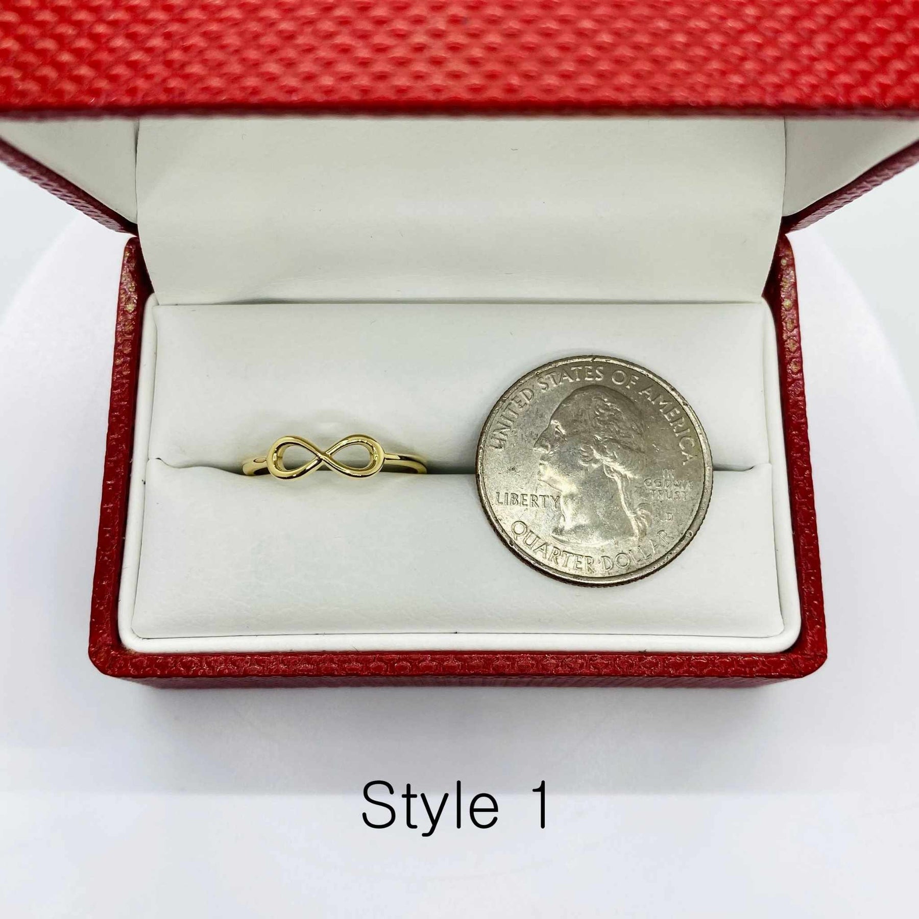 14k Gold ring with infinity symbol next to a quarter coin in a red jewelry box.