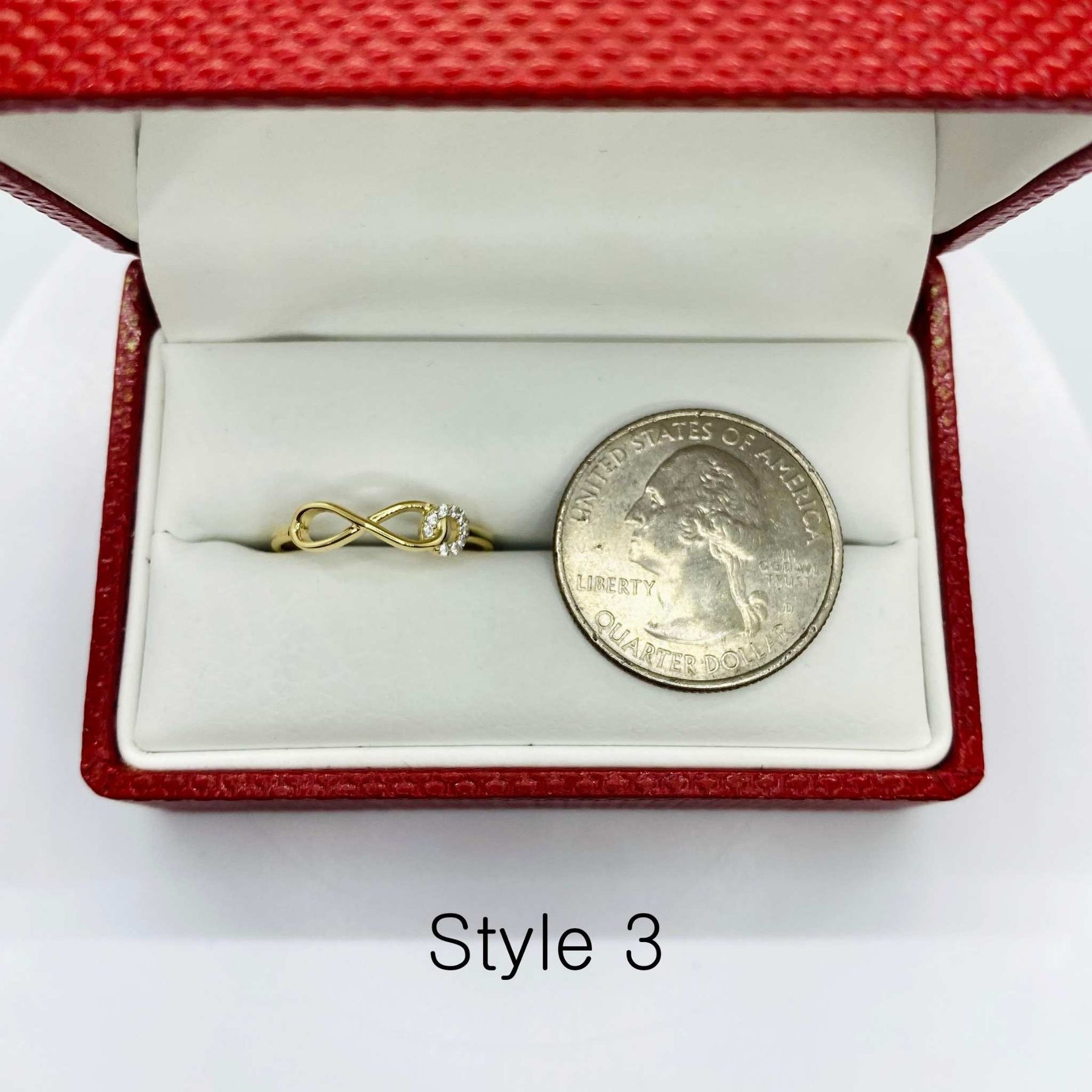 14k Gold ring with a Infinity design next to a coin in a red jewelry box labeled Style 3