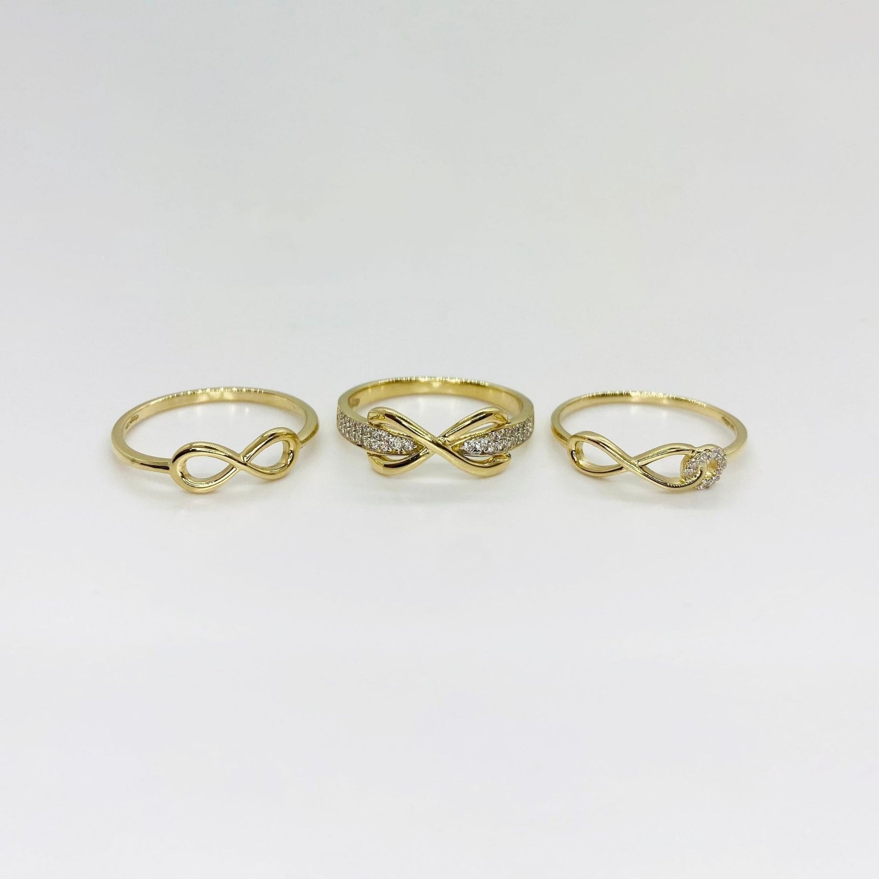 Three 14k gold rings with different infinity designs on a light gray background