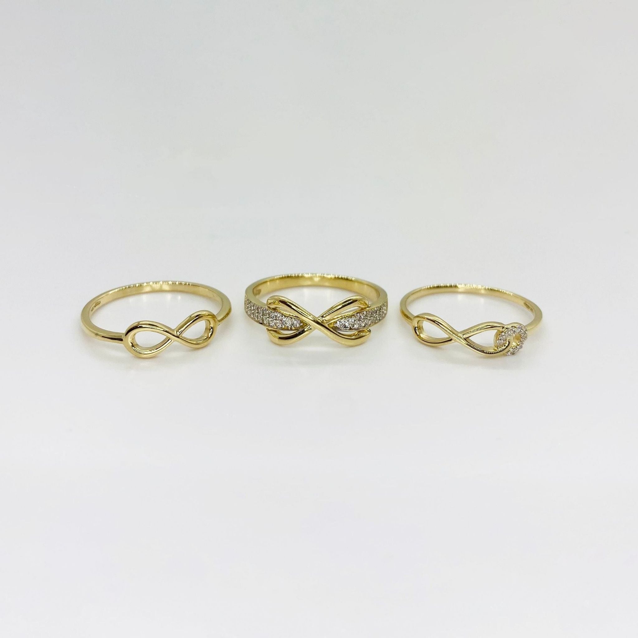Three 14k gold rings with different infinity designs on a light gray background