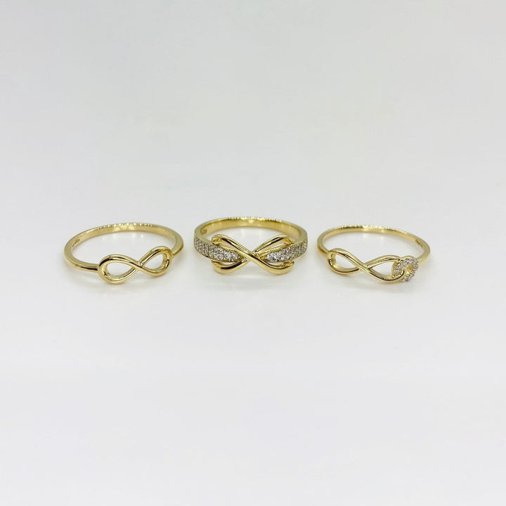 Three 14k gold rings with different infinity designs on a light gray background