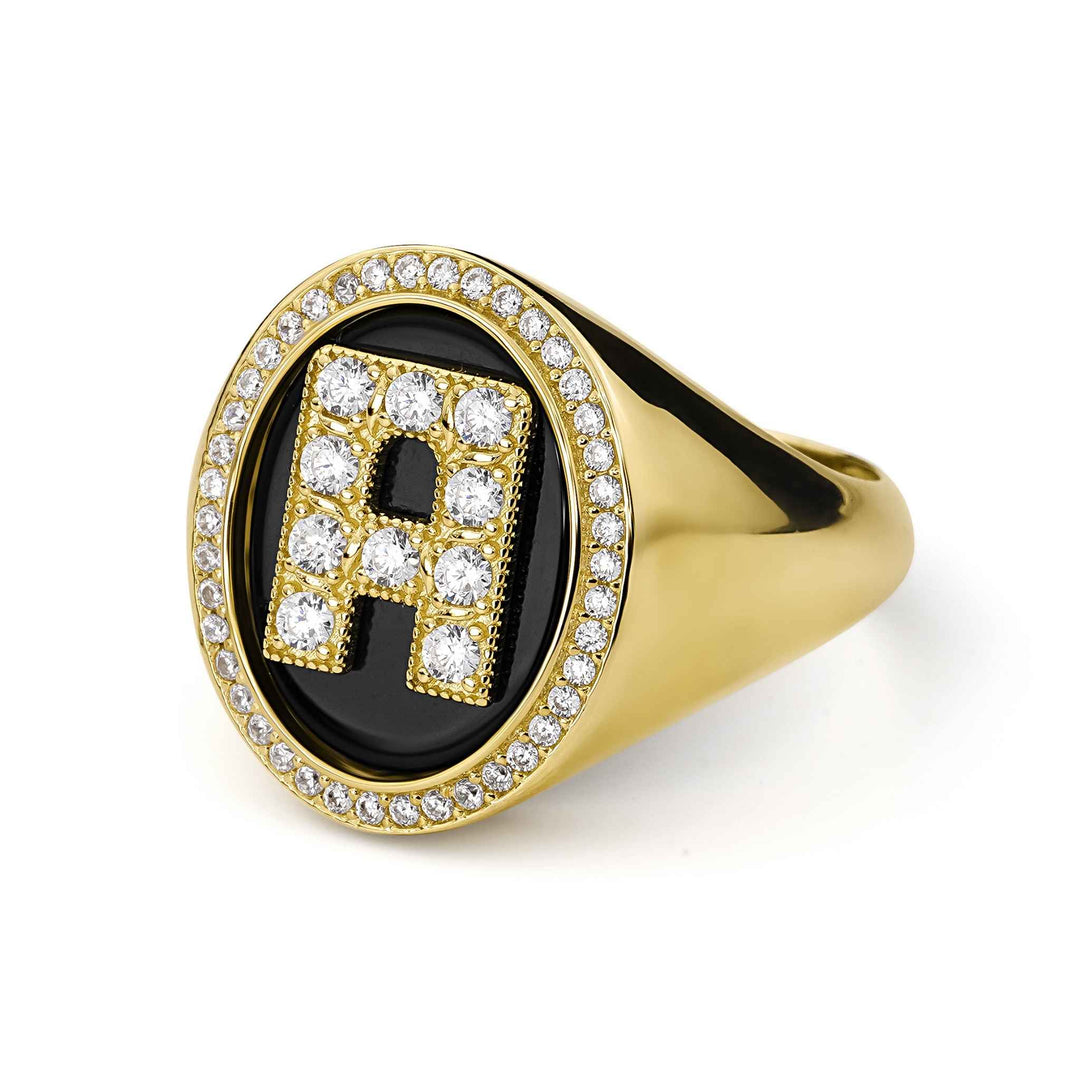 Angled view of a yellow gold signet ring with a crystal-paved letter "A" on black onyx.