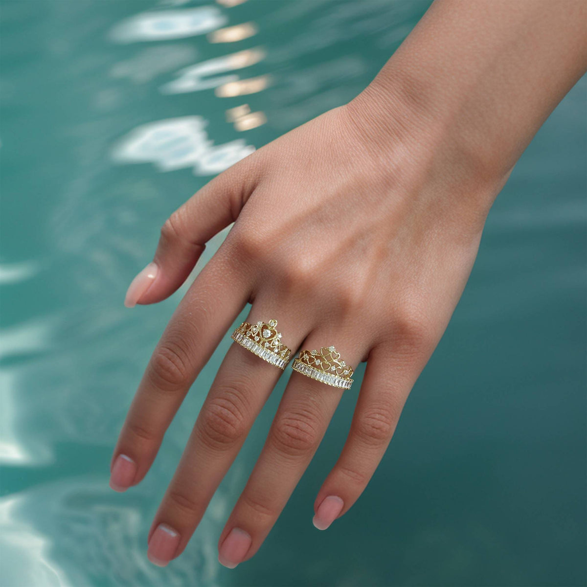 Pair of 14k gold crown band rings displayed horizontally against a tropical water backdrop.