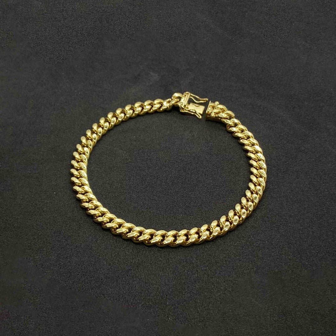 Polished 14k gold hollow Miami Cuban chain bracelet with box lock clasp on black background.