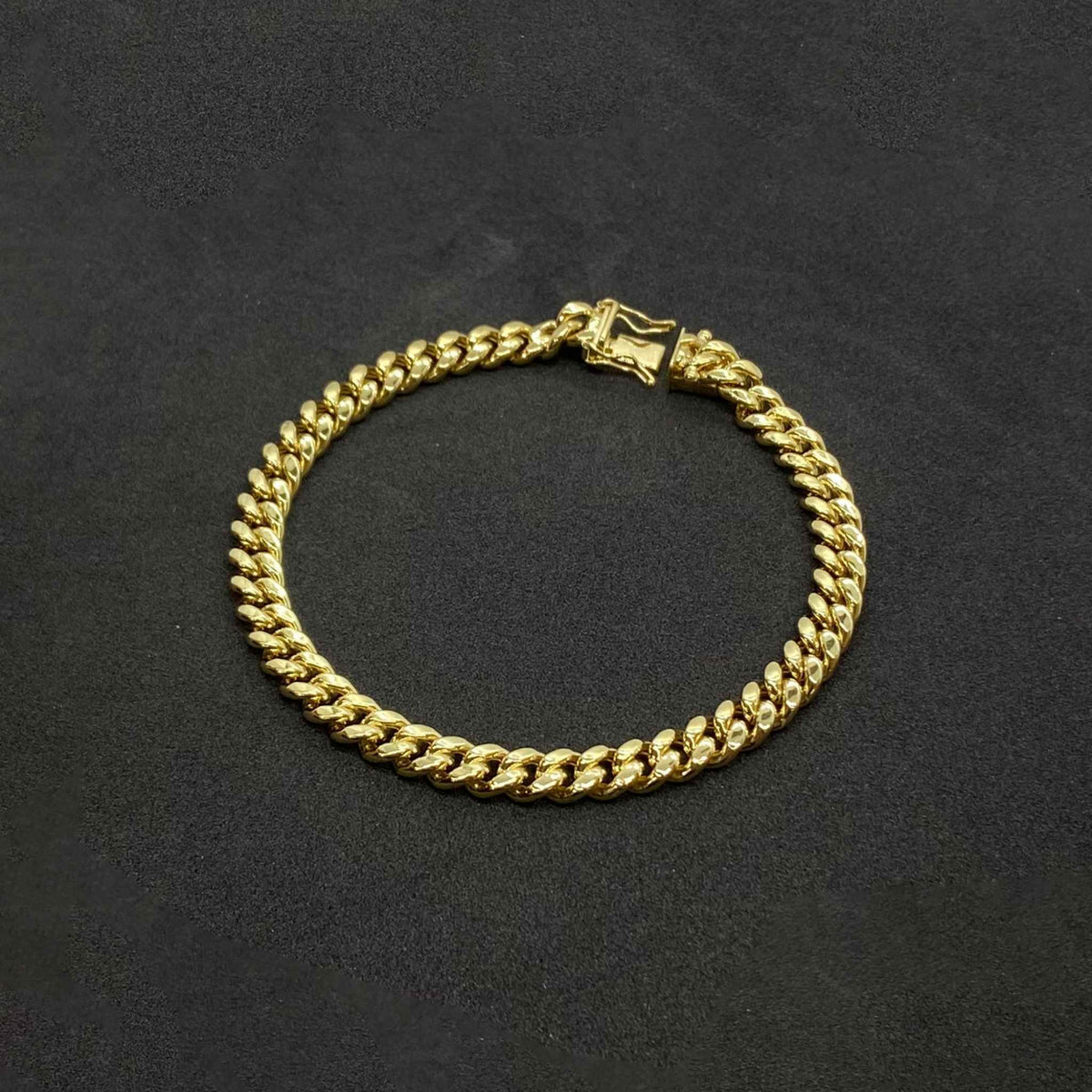 Polished 14k gold hollow Miami Cuban chain bracelet with box lock clasp on black background.