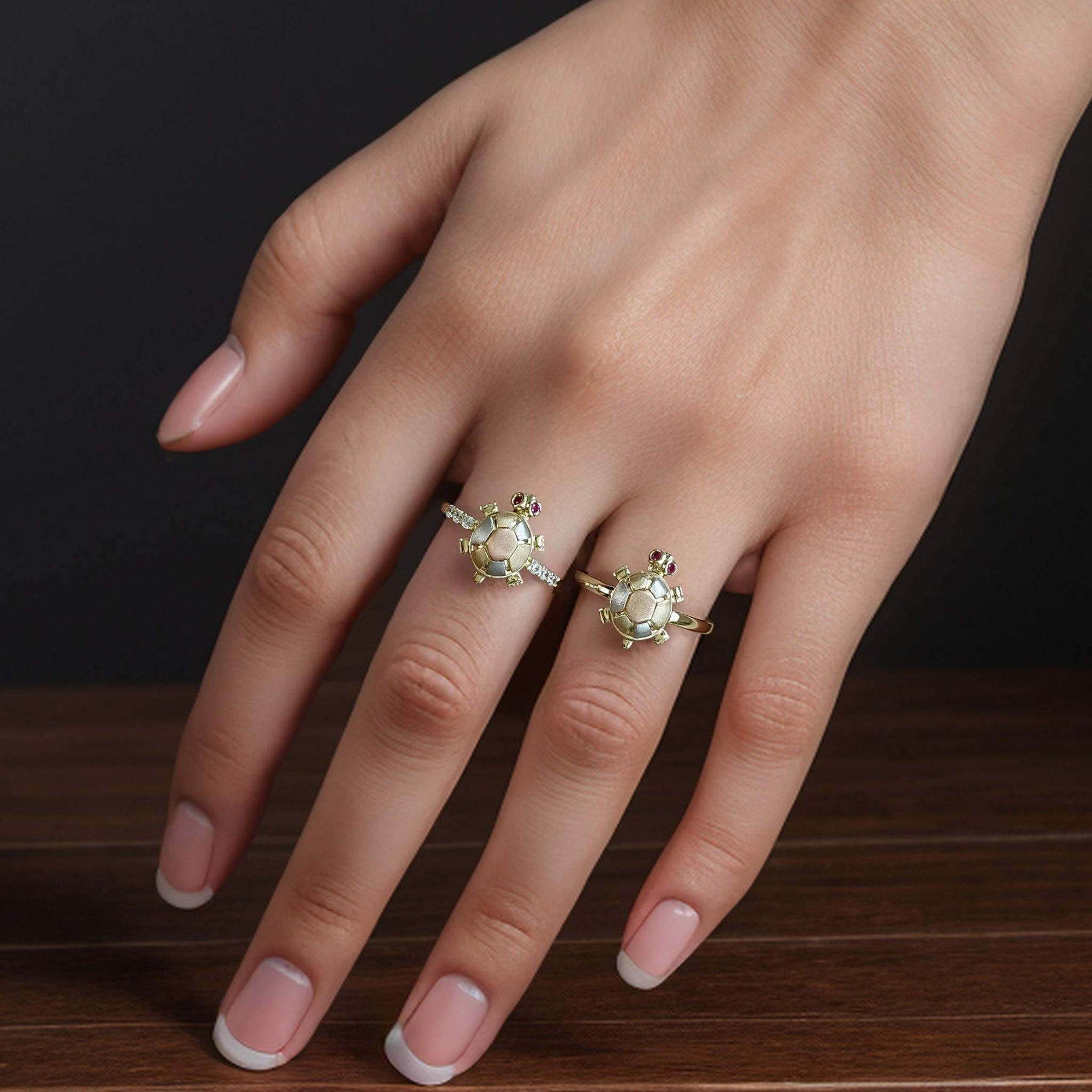 Two polished multi-toned gold turtle rings stacked beautifully on a manicured hand.