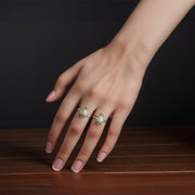 A woman’s hand wearing two tri-color gold turtle rings on a wooden surface.