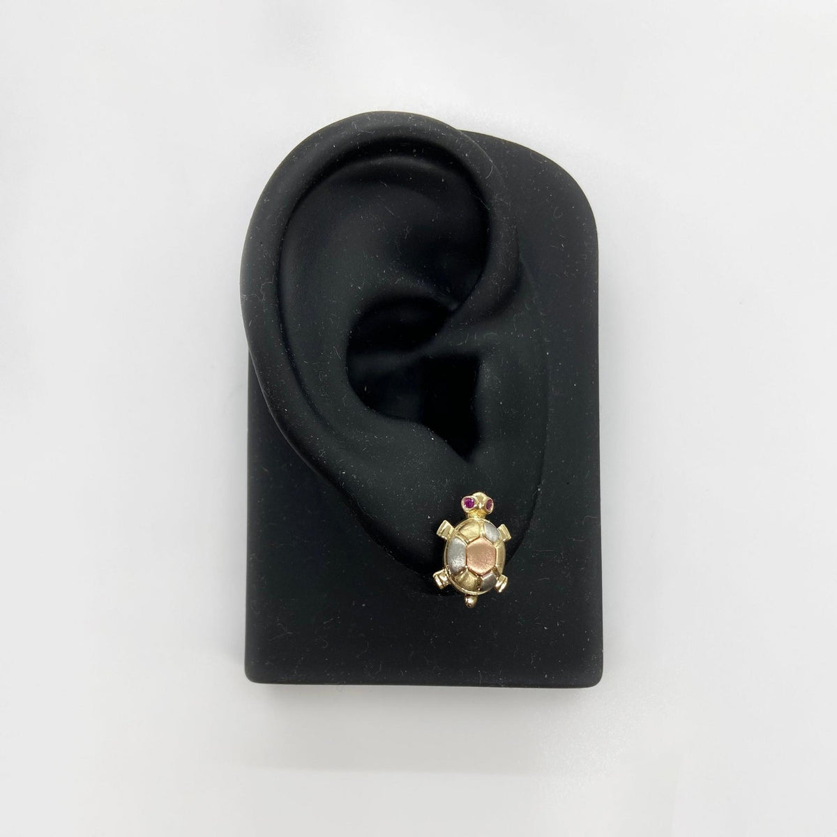 Gold turtle-shaped earring on a black ear model with a white background.