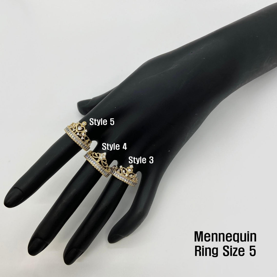 Black mannequin hand wearing three 14k gold crown rings with three different styles