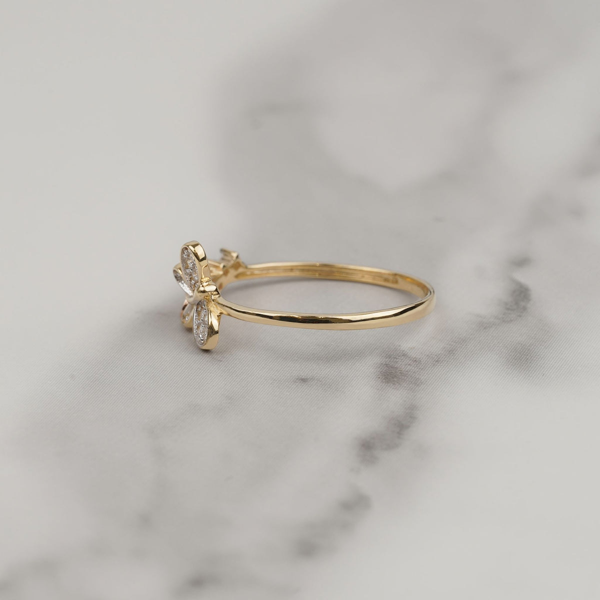 Side view of a 14k yellow gold butterfly ring resting on white marble.