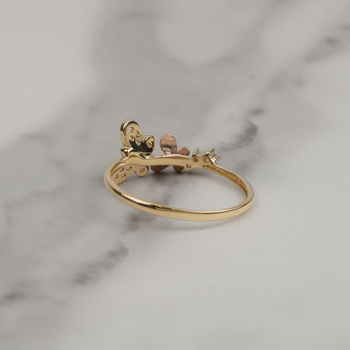 Back view of a 14k gold butterfly ring resting on gray marble.