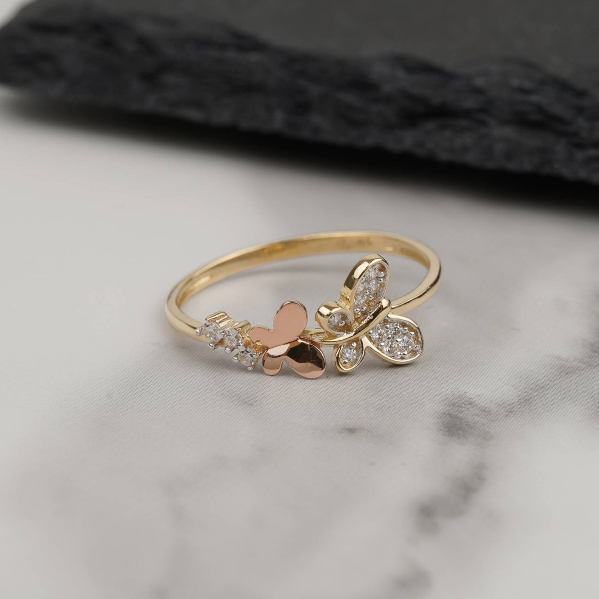 Dainty two-tone 14k gold butterfly ring with cubic zirconia on white marble.