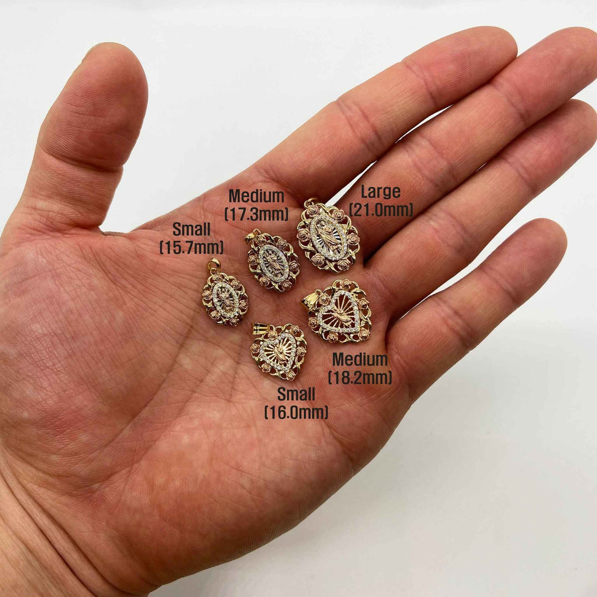 Five 14k gold Saint Jude pendants held in an open palm showing size options.