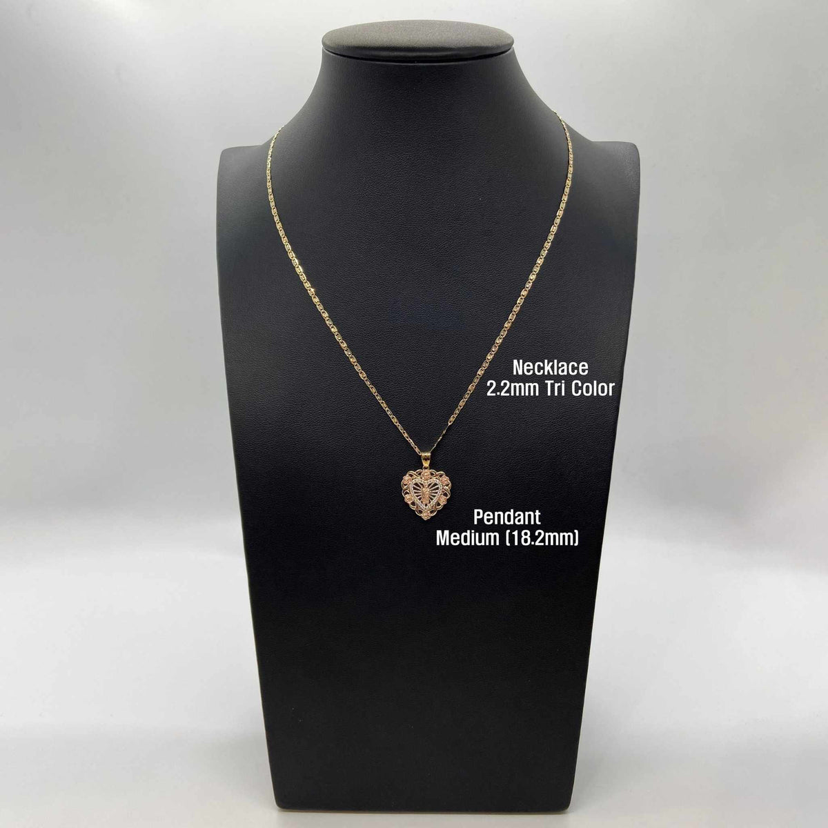 Gold heart pendant necklace on a mannequin display labeled medium 18.2mm and 2.2mm tri-color chain