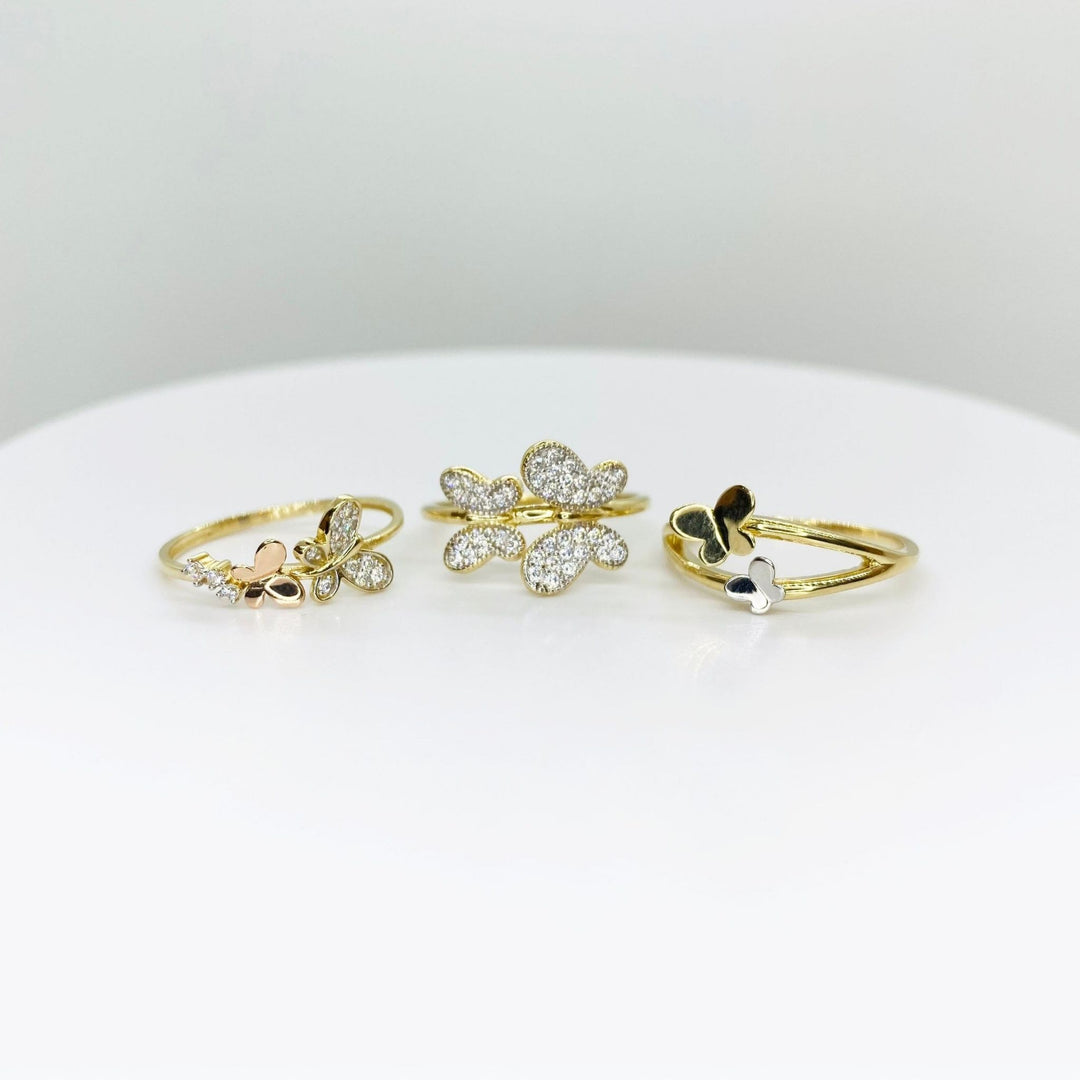 Three 14k gold rings with butterfly designs and three different style on a white surface