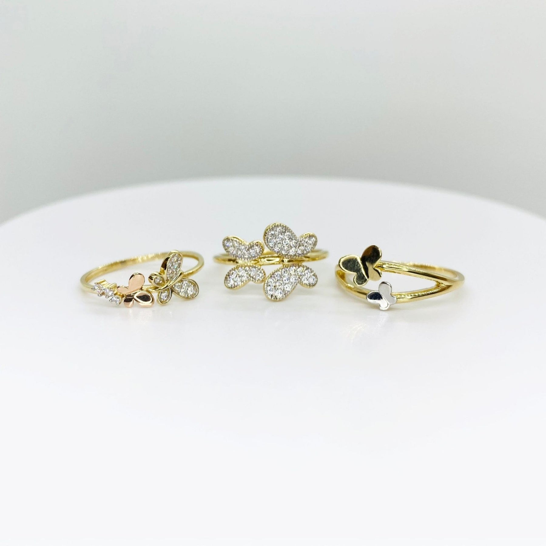Three 14k gold rings with butterfly designs and three different style on a white surface