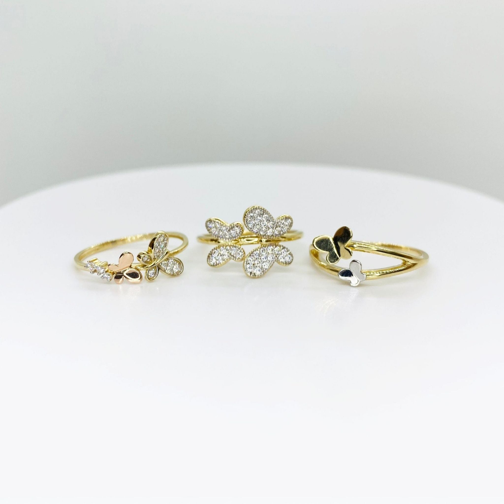 Three 14k gold rings with butterfly designs and three different style on a white surface