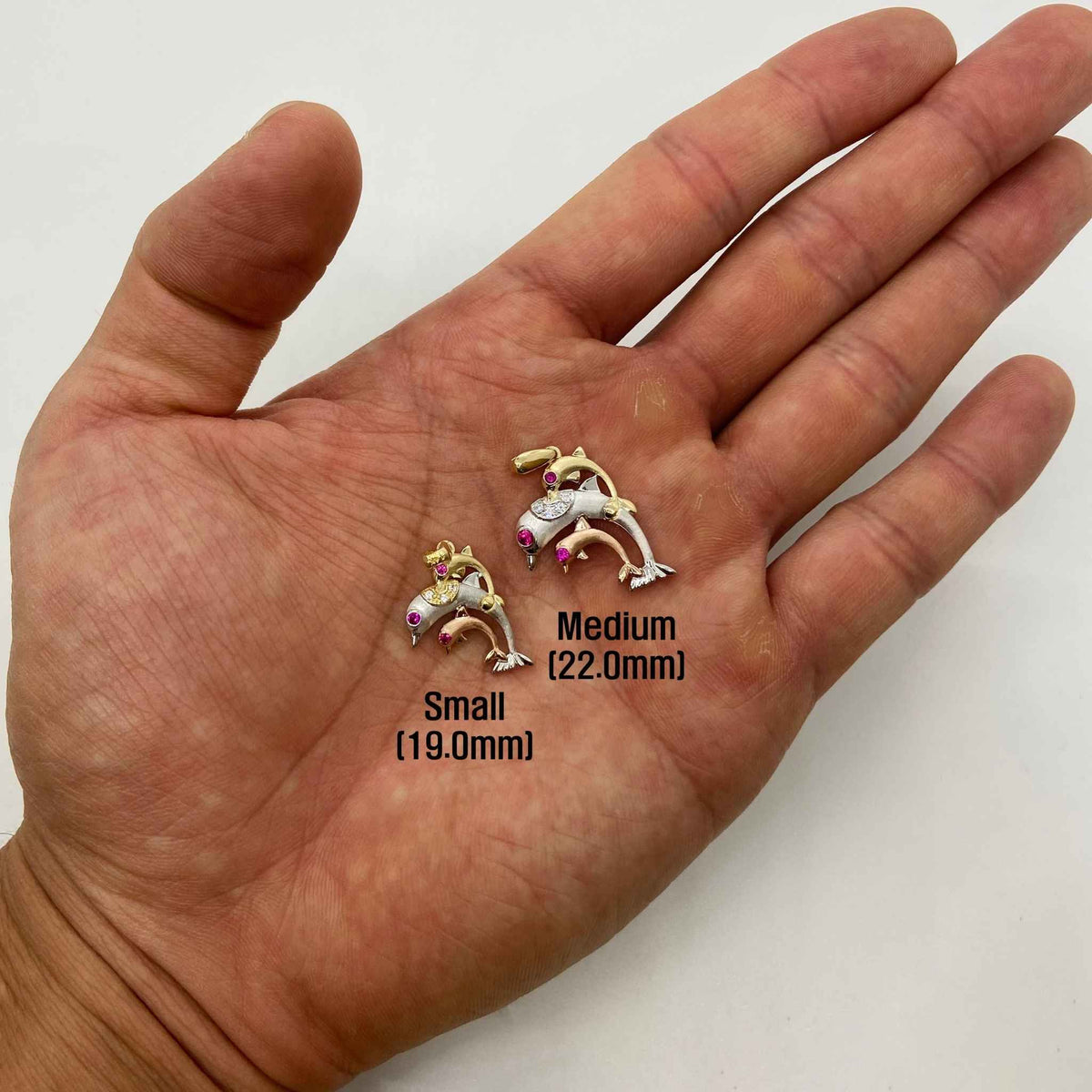 Small and medium 14k tri-color gold trio dolphin pendants resting on an open palm.