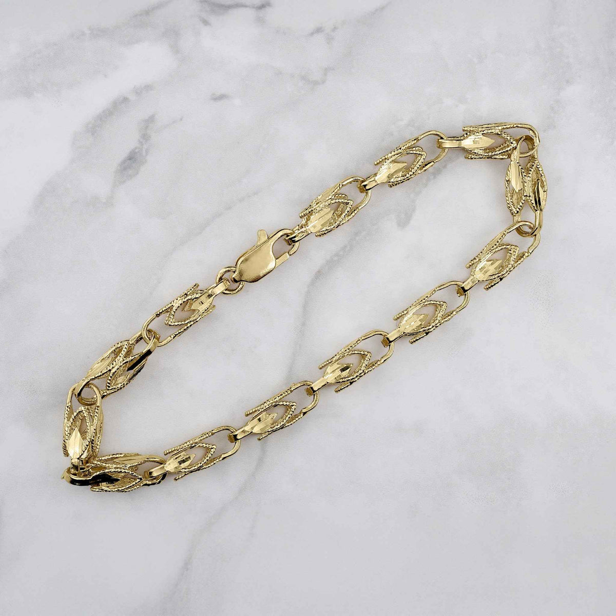 Textured 14k yellow gold Turkish link bracelet with a lobster clasp on marble.