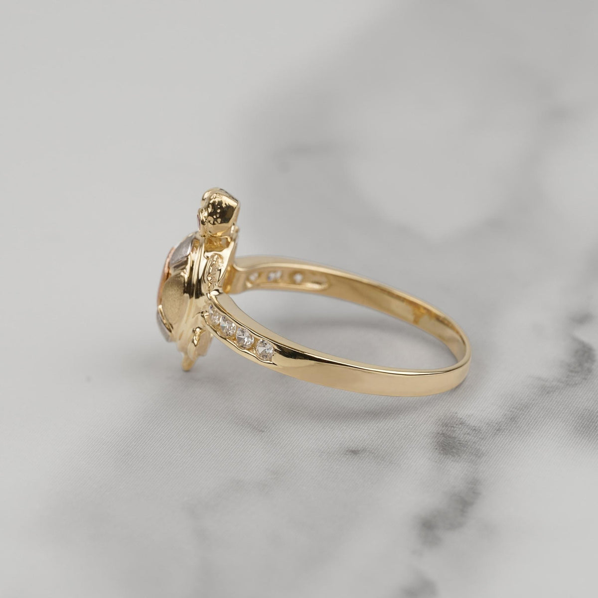 Side view of a gold turtle ring with CZ pavé band on marble.