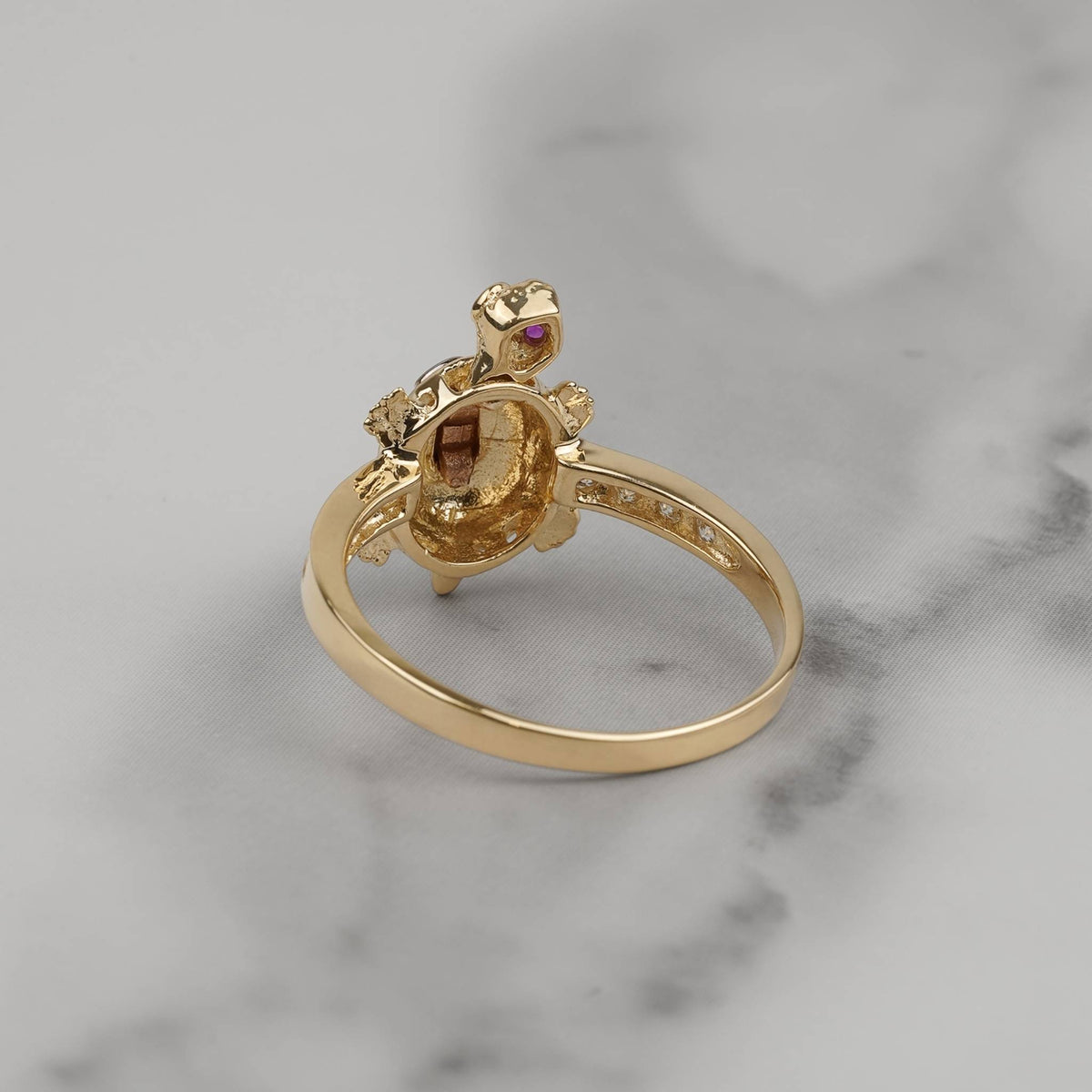 Back view of a gold turtle ring showing textured underside on gray marble.