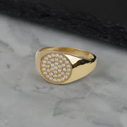 Men's yellow gold round signet ring featuring paved pave CZ on marble background.