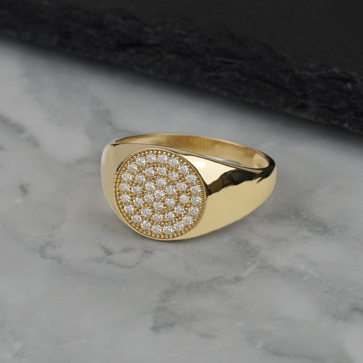 Men's yellow gold round signet ring featuring paved pave CZ on marble background.