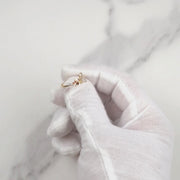 Gloved hand holding a 14k gold butterfly ring over a white marble background.